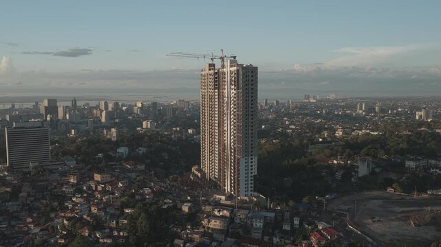 Aerial view of a tall skyscraper under construction with a crane on top, overlooking the dense urban landscape and residential houses in Cebu City, Central Visayas, Philippines.