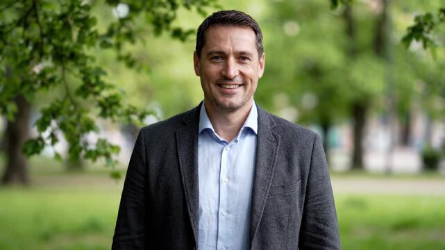 Middle Half Portrait of a happy mature businessman smiling at the camera in a green summer park, wearing an elegant jacket and shirt. Business success, confidence and healthy lifestyle concept.
