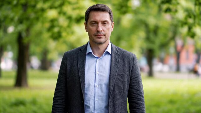 Portrait of a serious mature businessman looking at the camera in a green summer park, wearing an elegant jacket and shirt. Business success, confidence and healthy lifestyle concept.
