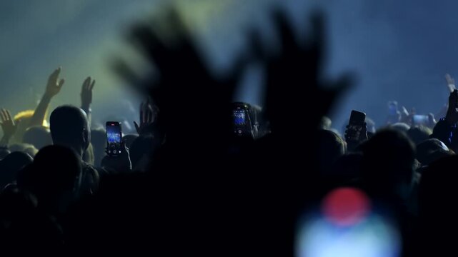 Crowd at a music concert recording performance with phones and waving hands
