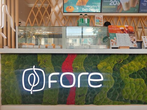 Illuminated logo Fore Coffee shop branding displayed on a modern cafe counter with pastry showcase and decorative green wall