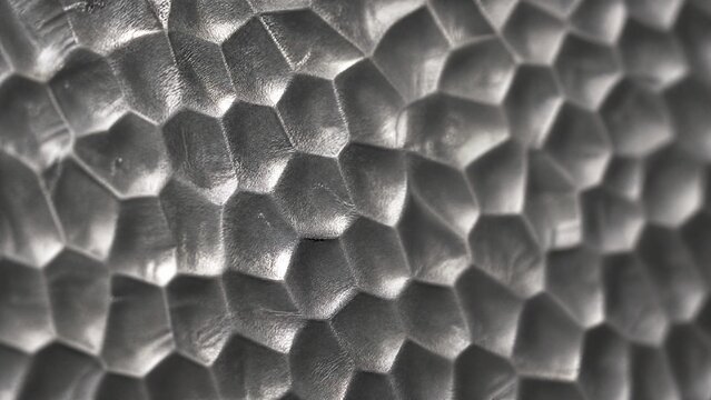 Close-up of a hammered tin sheet showing geometric dimple texture with dramatic shadows.
