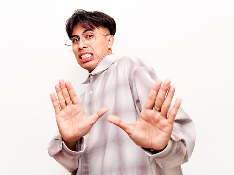 Disgusted young Asian businessman showing stop gesture with both hands to reject or avoid something, corporate refusal concept isolated on white background