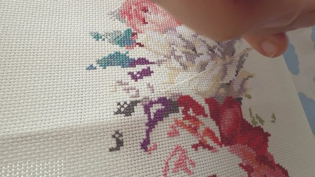 A woman using a needle and thread to create a cross-stitch embroidery pattern on white canvas