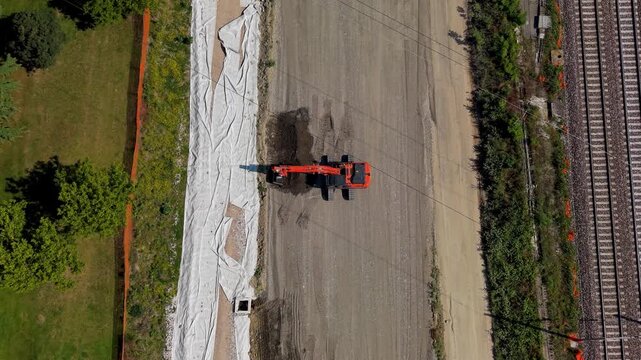Construction of the railway Aerial View: An aerial perspective showcases an orange construction vehicle at work on a large project, possibly paving or earthmoving