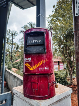 classic red metallic India Post letter box mounted on a concrete pillar with a padlock, showing the traditional yellow logo and bilingual text