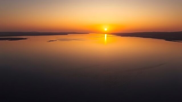 A wide river estuary at sunset with calm golden water reflecting the sky, serene.
