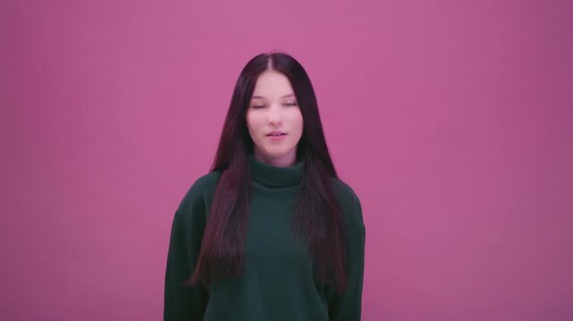 Portrait: teenage girl on pink background in green sweatshirt. Brunette woman face takes deep breath. Beautiful female, generation Z, alpha. Calm emotion and mindfulness, peaceful moment of relaxation