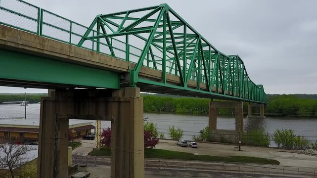Aerial drone video of a green railroad bridge going over river water and land with jib up camera movement.