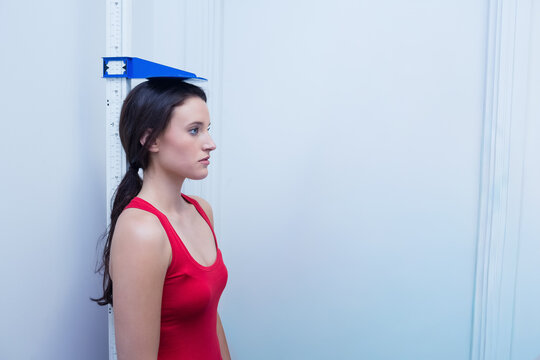 Adult female in red sleeveless top standing in profile with blue headpiece on stadiometer in clinic