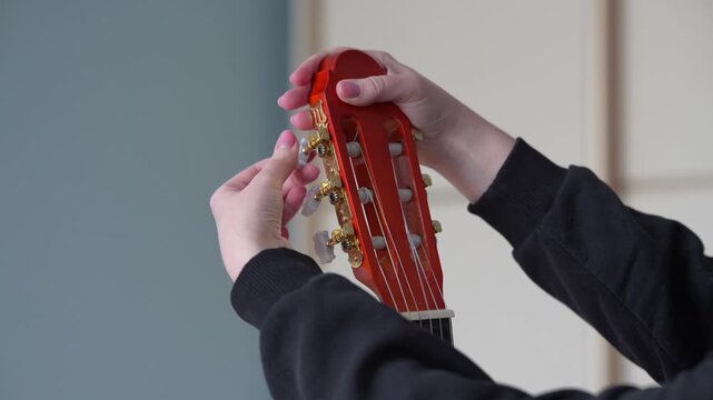 Close-up of female hand tuning guitar at home before playing