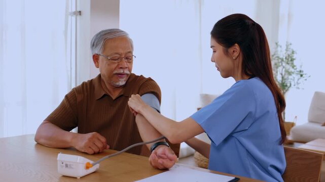 Caring young professional nurse checking blood pressure of calm asian senior man sitting at home for peaceful medical exam and health care