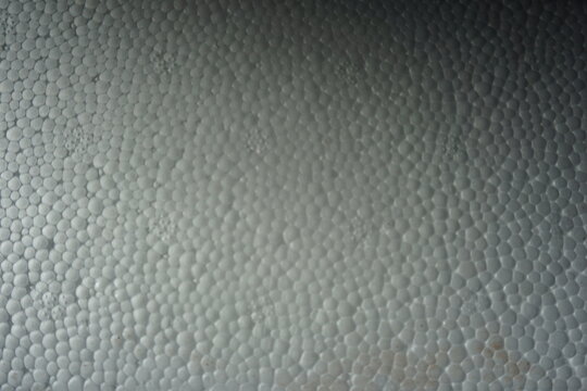 Macro shot of a white expanded polystyrene foam surface, showing the detailed cellular texture and structure. White plastic foam packaging material close-up.