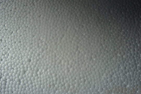 Macro shot of a white expanded polystyrene foam surface, showing the detailed cellular texture and structure. White plastic foam packaging material close-up.