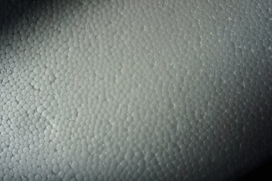 Macro shot of a white expanded polystyrene foam surface, showing the detailed cellular texture and structure. White plastic foam packaging material close-up.