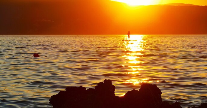 Man on a sailing board enjoys a magnificent orange sunset on the sea, summer sports background 