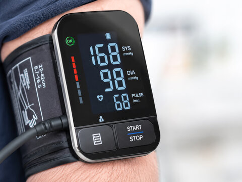 Close-up of a modern digital blood pressure monitor on a person's arm, displaying concerningly high systolic and diastolic readings (168/98 mmHg) and pulse rate, indicating potential hypertension or h