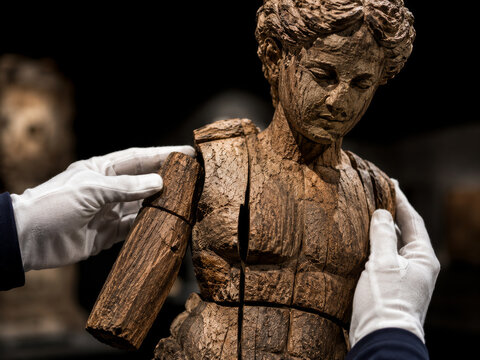 Expert hands in white gloves meticulously reassemble a beautifully crafted, ancient-looking wooden statue with intricate details, highlighting the delicate restoration process of a valuable historical