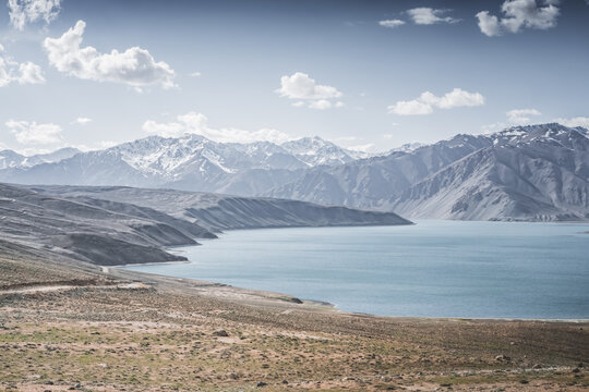 Landscape in the Pamir Mountains with a blue lake Yashilkul in the Tien Shan, a panoramic view of the highlands with snow-capped rocky peaks and the blue waters of the lake