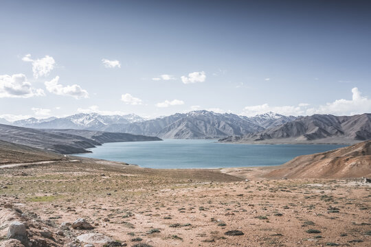 Landscape in the Pamir Mountains with a blue lake Yashilkul in the Tien Shan, a panoramic view of the highlands with snow-capped rocky peaks and the blue waters of the lake