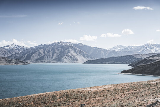 Landscape in the Pamir Mountains with a blue lake Yashilkul in the Tien Shan, a panoramic view of the highlands with snow-capped rocky peaks and the blue waters of the lake