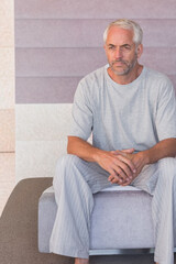 Fototapeta premium Man sitting on low ottoman wearing gray tee and striped pants inside lobby with tiled wall