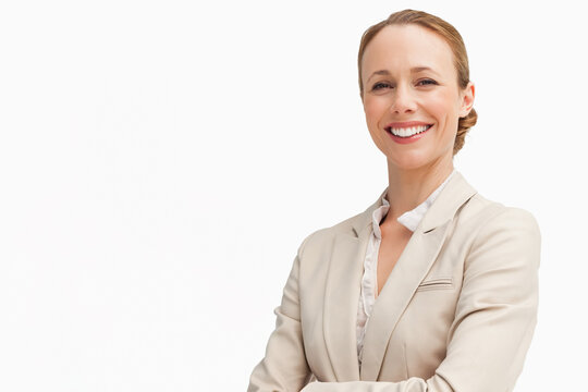 Female exec standing arms crossed, smiling in studio, wearing beige blazer white blouse, copy space