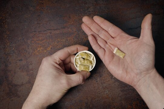 Cropped hands of man holding a box of  snus Nicotine pouches on dark background. 