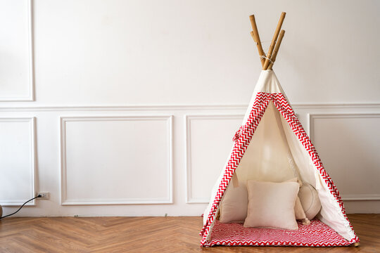 Cozy indoor teepee with red patterns, set against a white paneled wall.