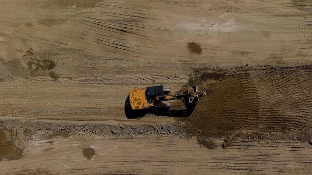 Aerial view of a yellow excavator standing during a work break at a new railway construction site, showing earthworks and major infrastructure development.