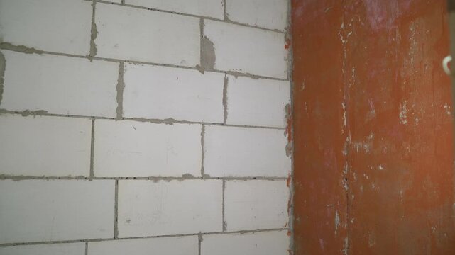 Close up of rough orange concrete column meeting white block wall. Industrial background showing construction materials and raw textures. Minimalist abstract composition with orange and grey colors