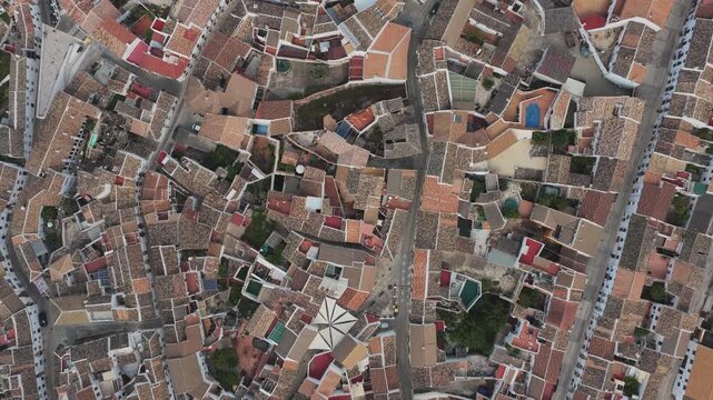 Aerial view of the dense terracotta rooftops and narrow streets of the historic white village of Zuheros, Andalusia, Spain.