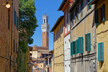 Fototapeta premium SIENA, ITALY, April 25, 2026 : Torre del Mangia of Palazzo Pubblico can be seen from the small streets of city center