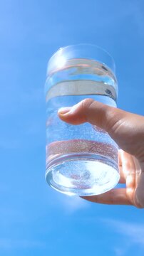 transparent glass glass of water with pure mineral water in hand against the sky with bright glare of the sun