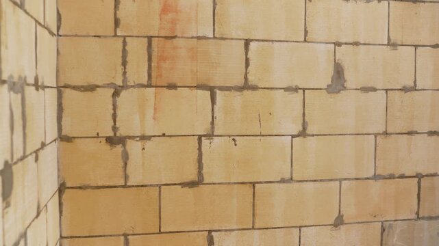 Industrial background of aerated concrete block wall during construction. Yellow waterproofing primer applied to porous surface, creating abstract grunge texture with drips