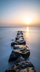 Obraz premium Experience tranquility with this long exposure coastal landscape. Stone rocks lead into a misty sea under a golden sunrise, symbolizing focus, paths, and inner peace in wild nature.