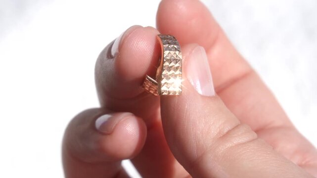 The bright sparkle of a gold earring in a woman's hand