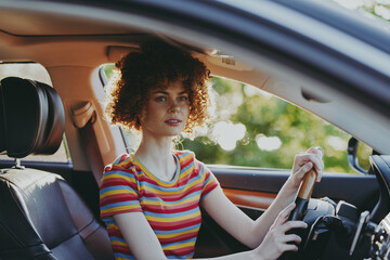 Fototapeta premium A young woman sits in a colorful striped shirt in a car, a casual, relaxed portrait captured in warm retro tones. A lifestyle moment highlighting everyday travel and self expression.