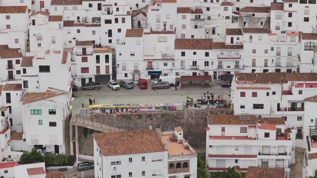 Aerial view of the traditional white-washed houses and central square with parked cars and people in the hillside village of Casares, Andalusia, Spain.