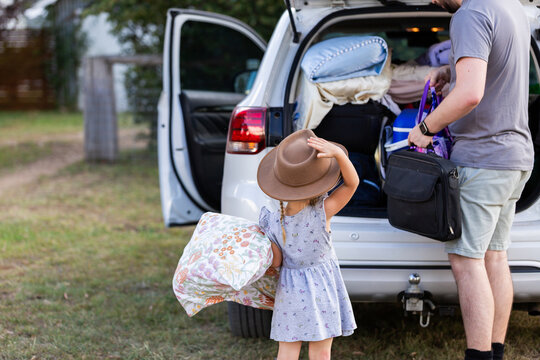 child helping dad unload back of car packed with luggage for farmstay trip