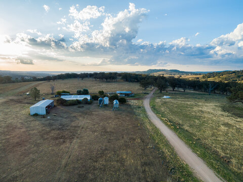 Soft sunset light over farm sheds and silos beside gravel road