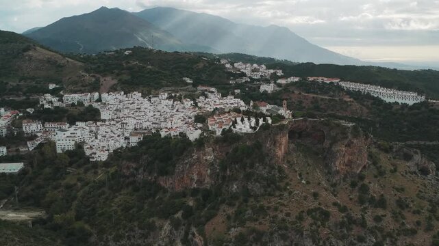 Aerial view of the white village of Casares perched on a cliffside with traditional houses and green mountains under a cloudy sky Casares, Andalusia, Spain.