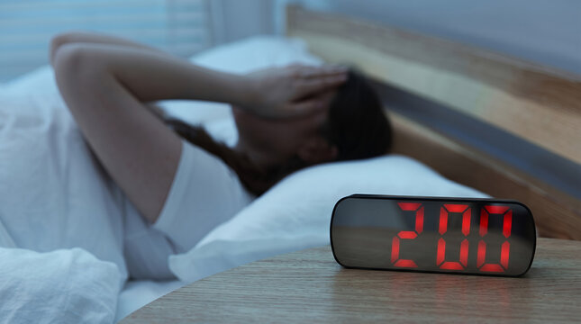 Woman feeling stressed with a clock showing 2:00 in a dark bedroom
