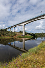 Fototapeta premium Railway viaduct spanning river reflecting under cloudy sky