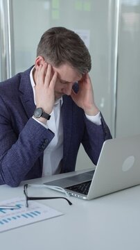 Businessman slumped at his office desk, rubbing his temples from headache and digital eye strain, exhausted and overwhelmed by work pressure and professional burnout
