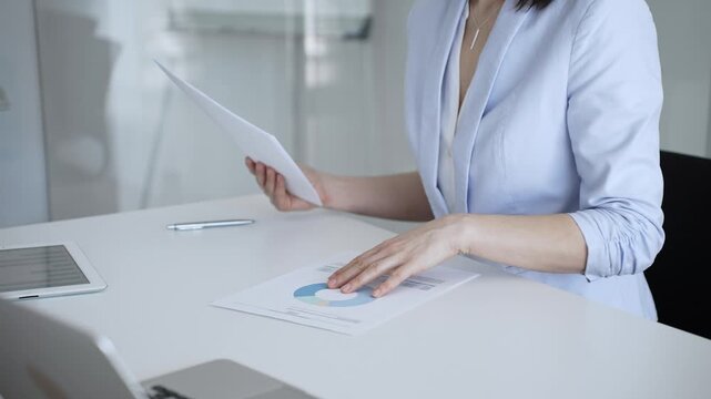 Businesswoman analyzing financial data and reviewing charts on reports, managing paperwork and accounting documentation in a modern office, planning business strategies