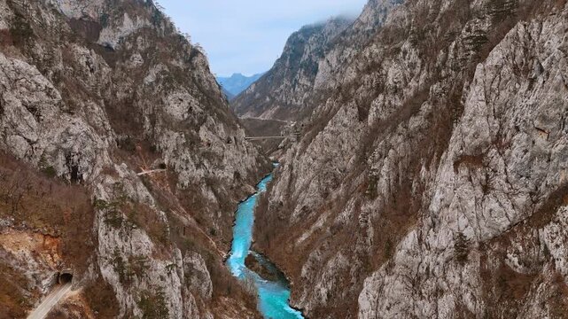 Wide aerial view of deep limestone canyon with turquoise river and bridge. Steep limestone walls frame the full canyon width as the turquoise river flows below and a bridge spans the gorge ahead.