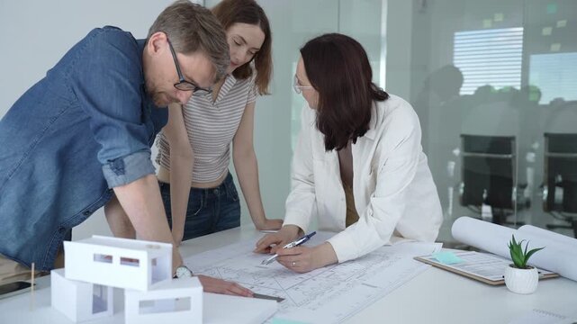 Group of architects discussing building blueprints and a structural model, collaborating on an urban development project in a modern office environment. Architects at work