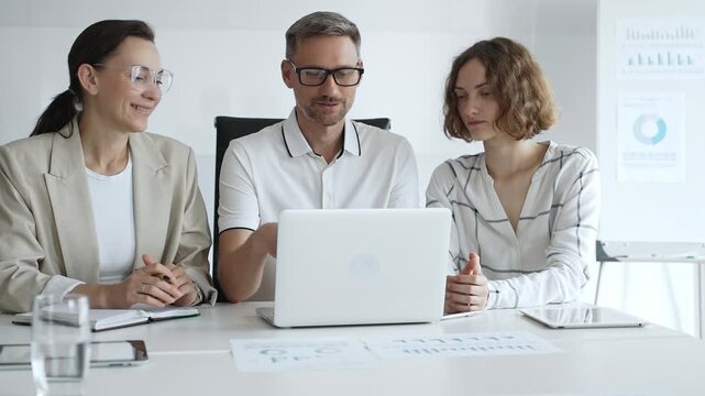 Professional team analyzing data on laptop, sharing insights during collaborative office meeting, highlighting workplace synergy and strategic planning