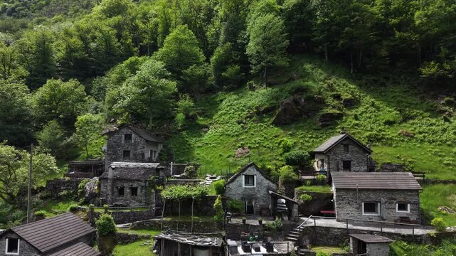 Aerial view of the historic stone houses of Corippo Albergo Diffuso nestled against a lush green hillside in Corippo, Ticino, Switzerland.